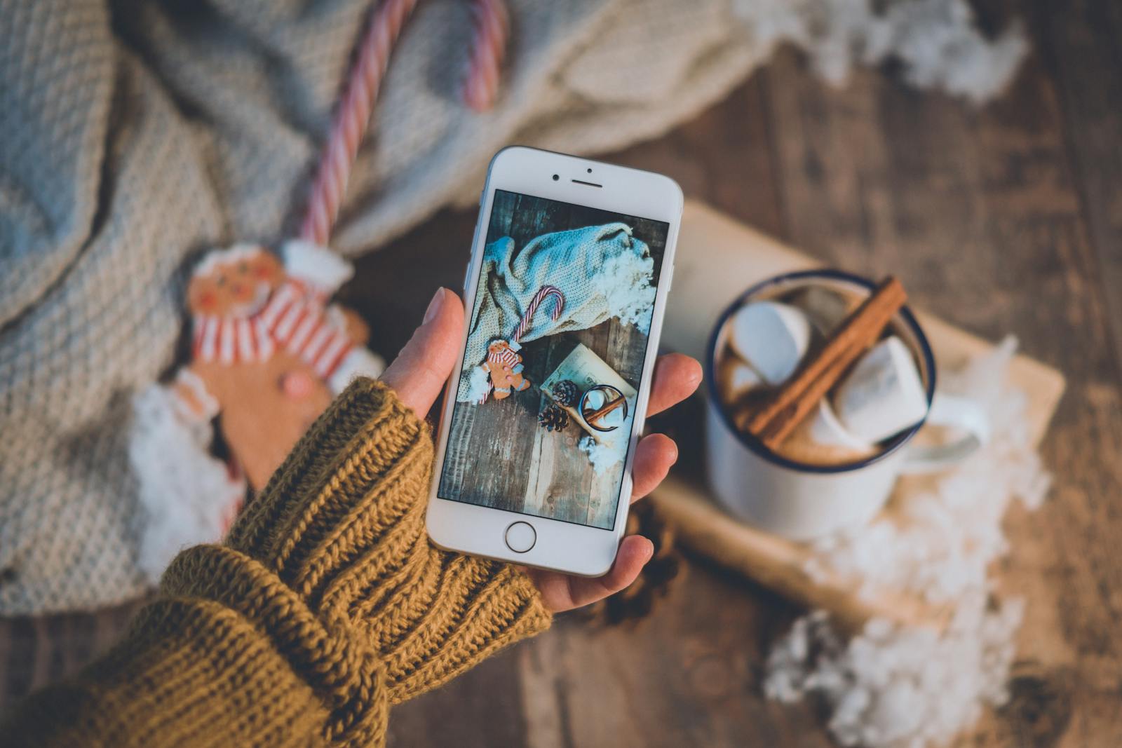 Warm winter scene with hot chocolate, knitted sweater, and smartphone in hand.