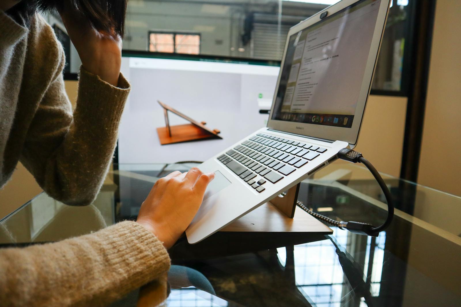 Woman working on a laptop with ergonomic stand in an office setting, focusing on productivity.