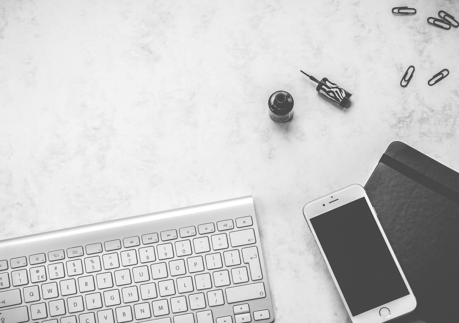 Black and white minimalist desk setup featuring a keyboard, smartphone, and stationery items.